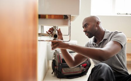 Young,Black,Male,Plumber,Sitting,On,The,Floor,Fixing,A